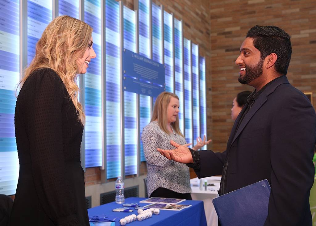 A man and woman having a discussion at an event, as two women do the same in the background.